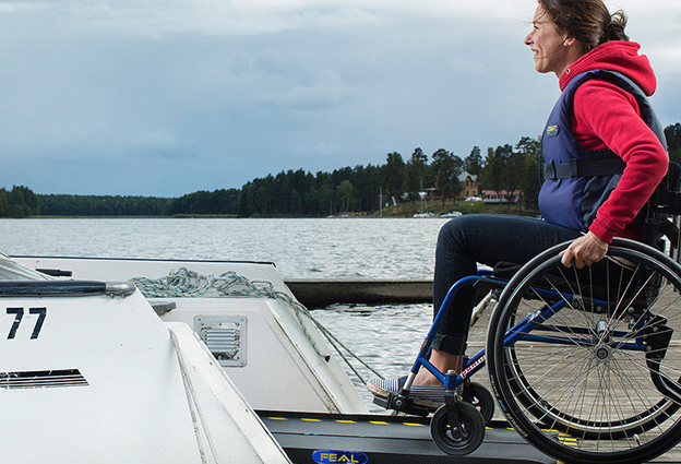 Kuvassa nainen pyörätuolissa on siirtymässä veneeseen.