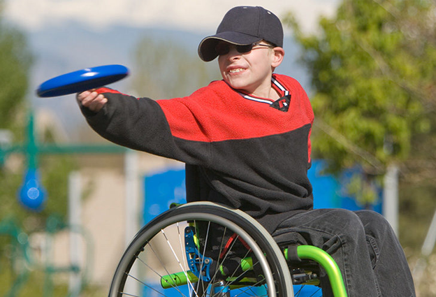 Poika heittää frisbeeta pyörätuolista